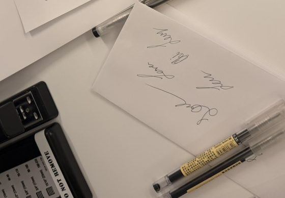 A scratch sheet covered in practiced signatures beside two pens on an office desk